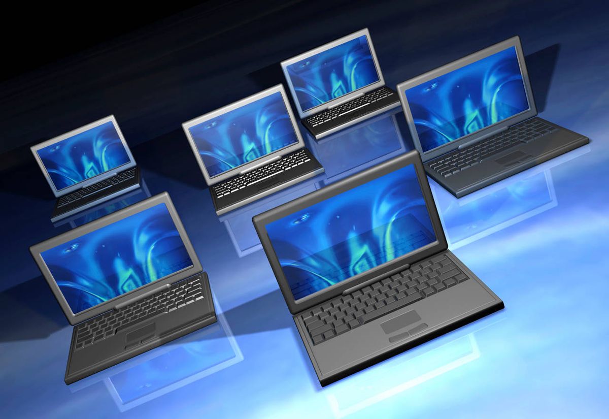 Multiple laptop computers arrayed on a reflective glass-like surface.