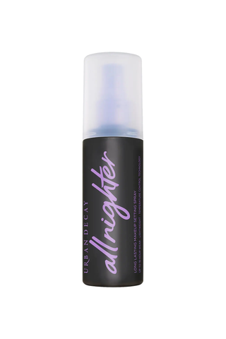 A black bottle of Urban Decay's All Nighter hairspray (written on the bottle in purple writing) against a white background.