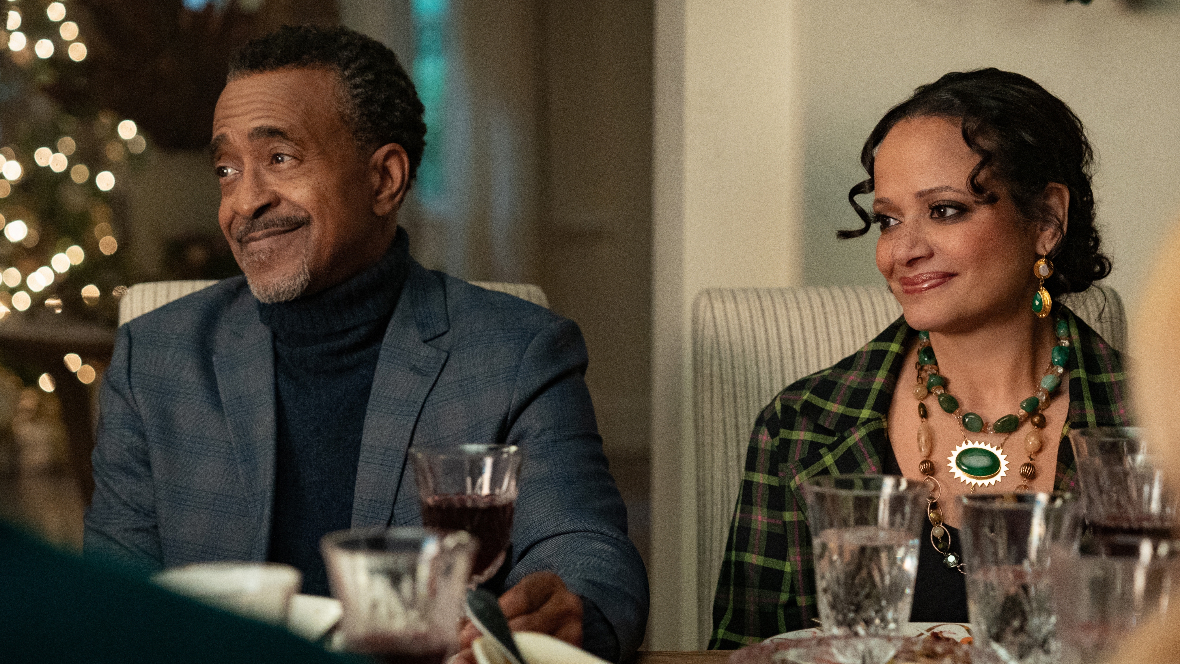 Tim Meadows as Stan and Judy Reyes as Margaret sitting at the Christmas dinner table and smiling in Our Little Secret.