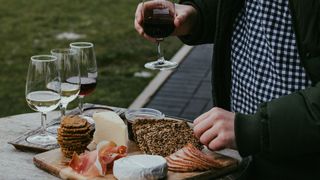 Plate of cheese and crackers, with glasses of red and white wine in the background. Man takes a glass of wine and some cheese.