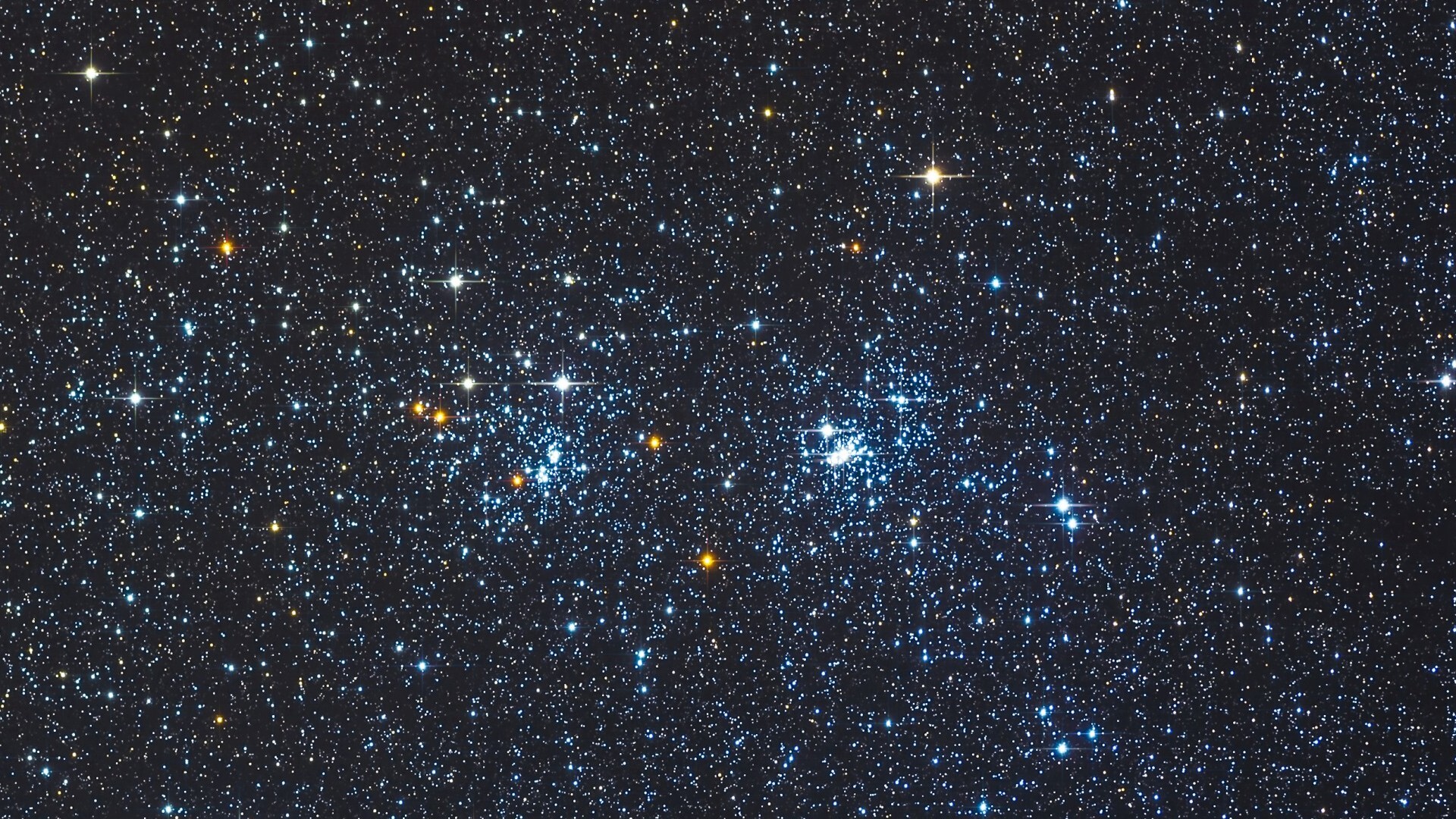 A deep space image showing two clusters of bright blue stars side by side against a more distant starfield peppered with red stellar bodies