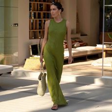 British female fashion influencer Jessica Skye poses on a modern outdoor patio wearing a low bun, yellow-gold earrings, woven leather tote bag, and green maxi dress