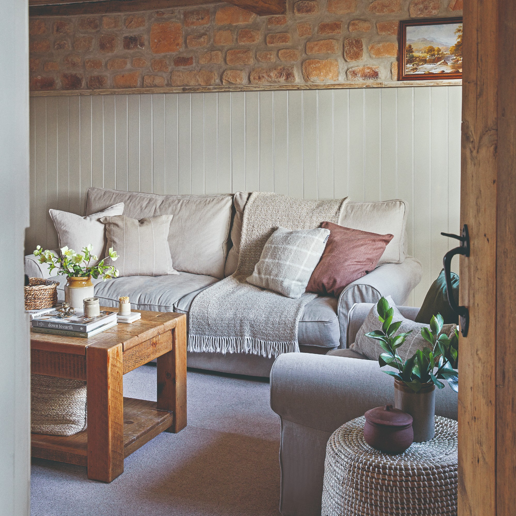 A cosy living room with a beige sofa layered with throws and cushions, a tonal armchair and a wooden coffee table