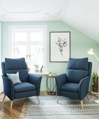 Pair of padded charcoal recliner chairs with wooden legs, in relaxed space with mint green wall, patterned mono rug, and mono botanical wall art.