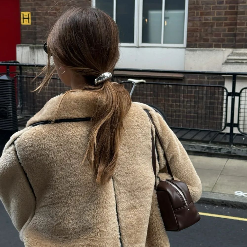 A woman wearing a shearling coat with a ponytail and a metal silver hair tie