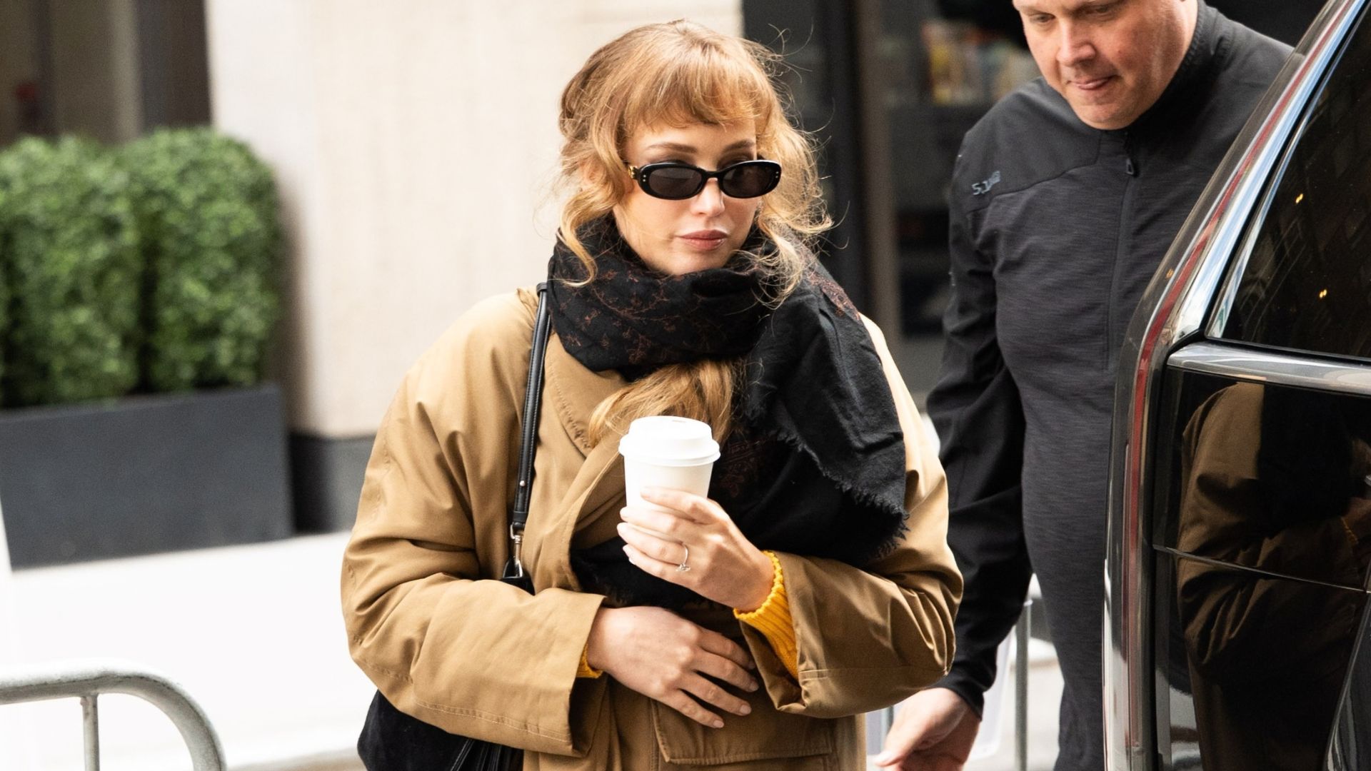 Jennifer Lawrence steps outside in New York wearing a beige trench coat with a black scarf, black sunglasses, grey jeans and Uggs.