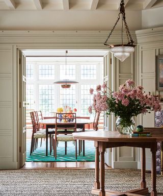 Entryway table with a vase of large pink flowers looking into a dining room