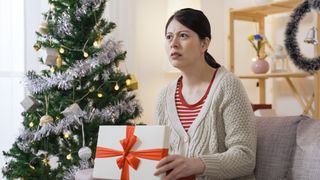 Woman holding gift box, looking dismayed by its contents