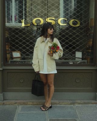 Tamara wears a canvas jacket white dress, and black sandals