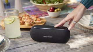 Harman Kardon Luna bluetooth speaker on a table, with a woman's hand pressing a button on it