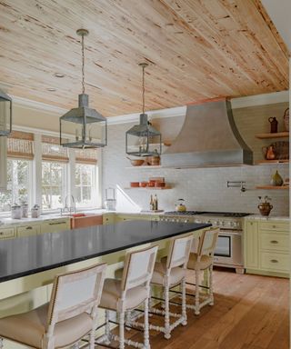 Welcoming, homely kitchen with coordinated wood floor and ceiling, and trio of lantern pendants hanging above island