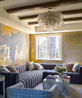 Living area with gray ridged sectional, metallic mural wallpaper and statement globe pendant