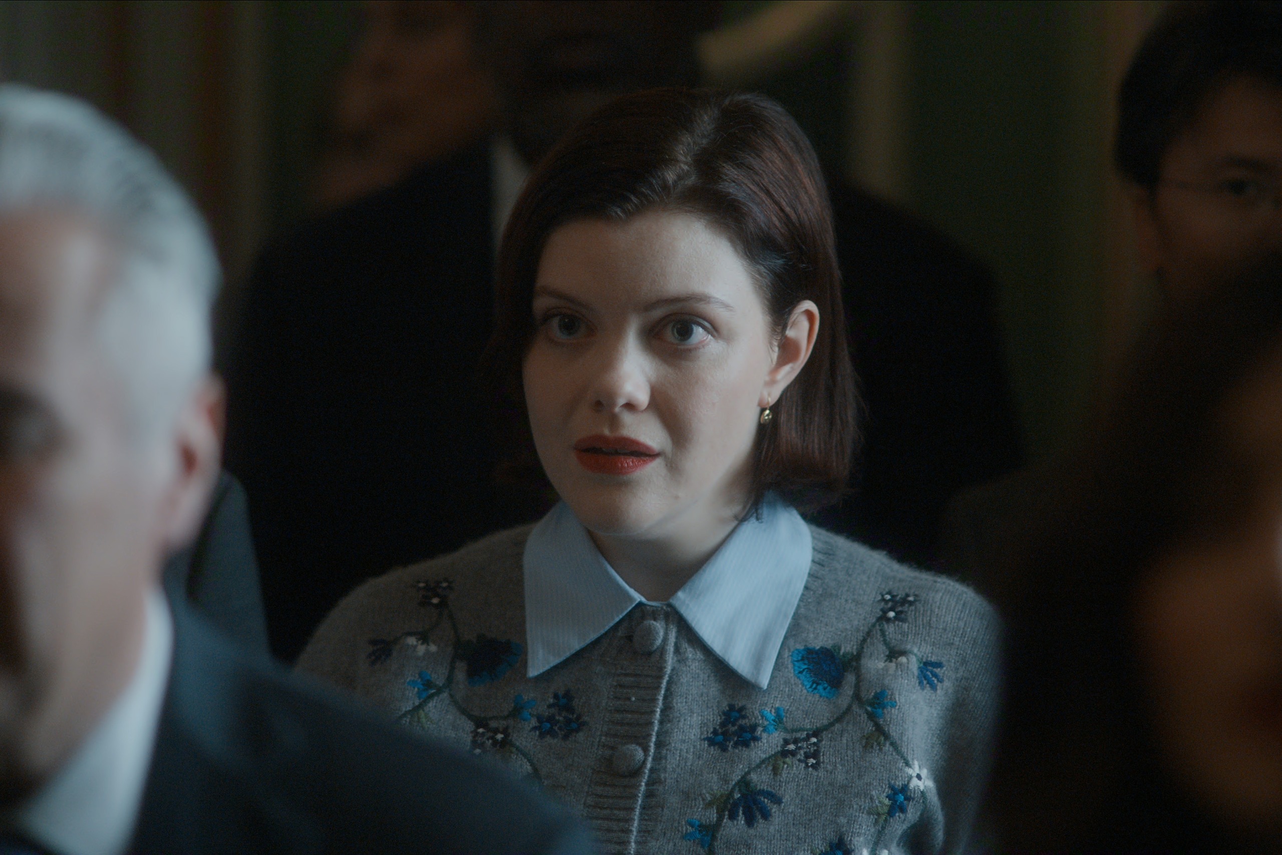 Georgie Henley as Pensy, standing among tall men in suits, in 'The Diplomat' season 4.