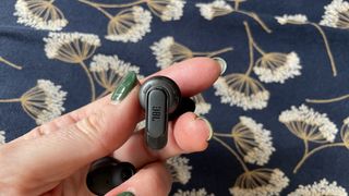 JBL Tour Pro 3 earbuds held in a hand, with navy floral background