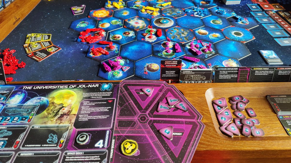 A closeup of Twilight Imperium fleet tokens, cards, and more laid out on a wooden surface