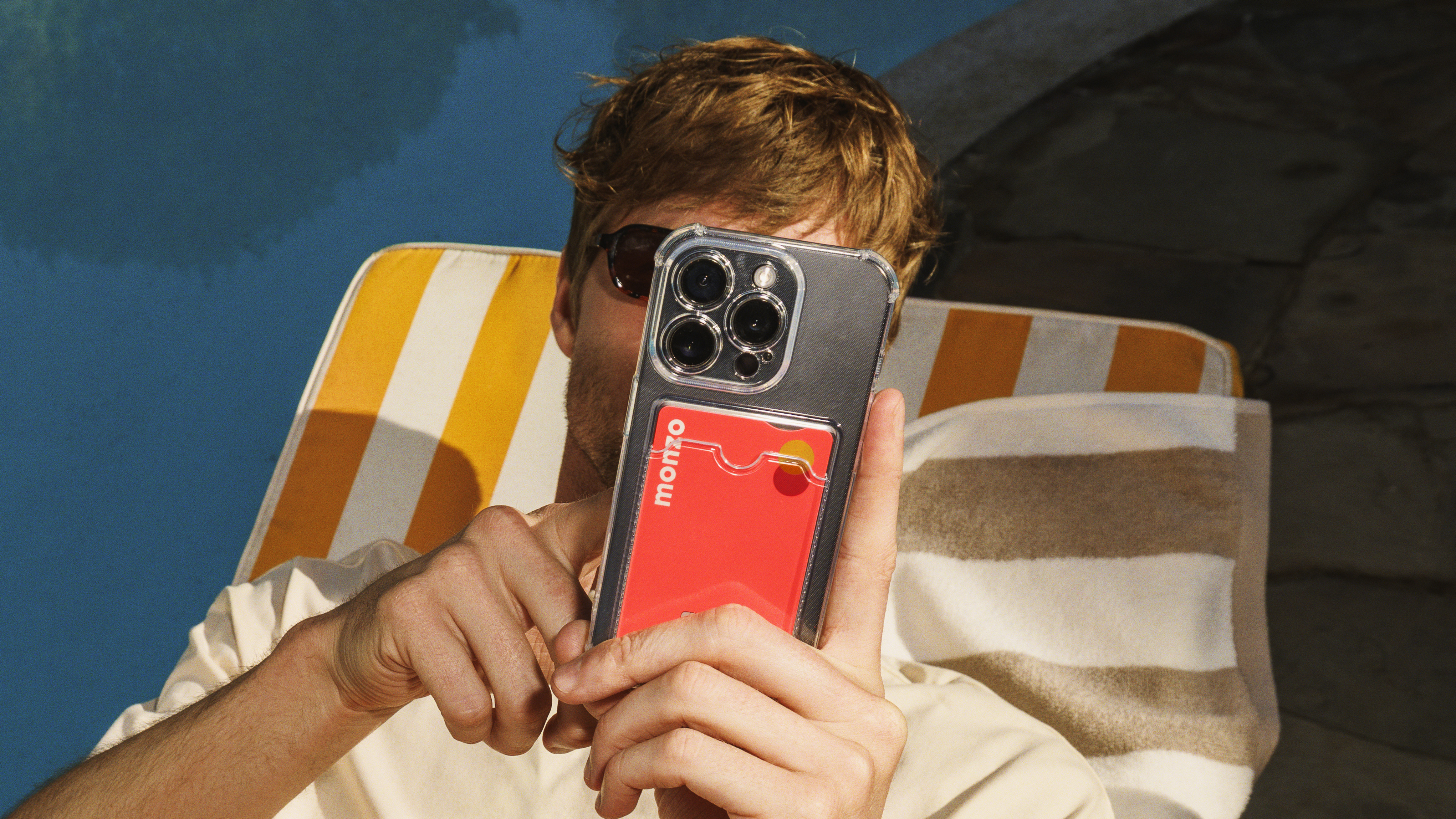 A man on a sun lounger using a phone with a Monzo card