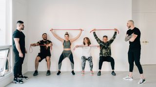 Check out our roundup of the best resistance bands. Here, a group of gym goers completes airbench with a resistance band around their hips for strength and stability.