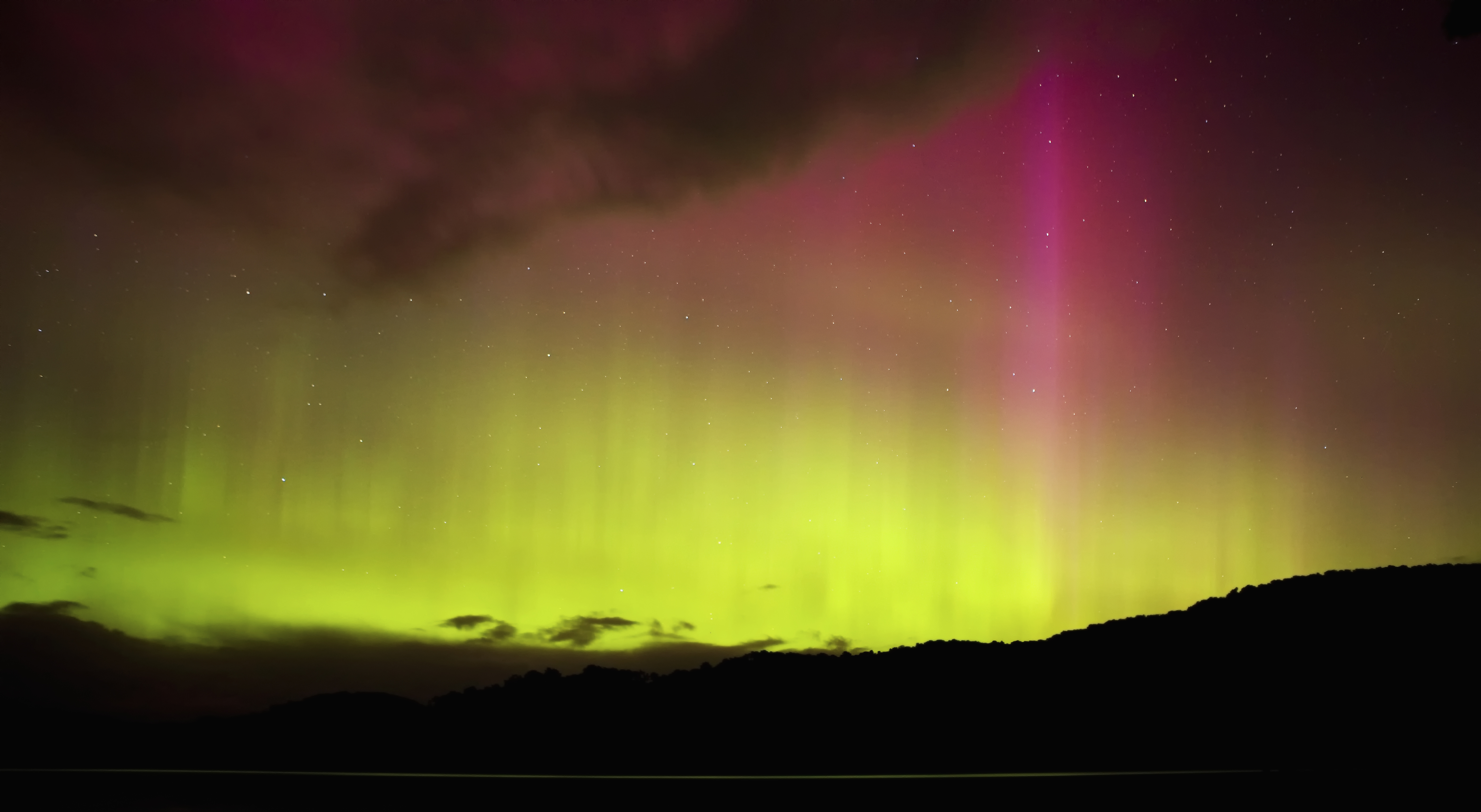 green and pink aurora over a dark horizon