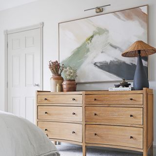 a double wooden chest of drawers beneath a large piese of wall-hung art in a bedroom