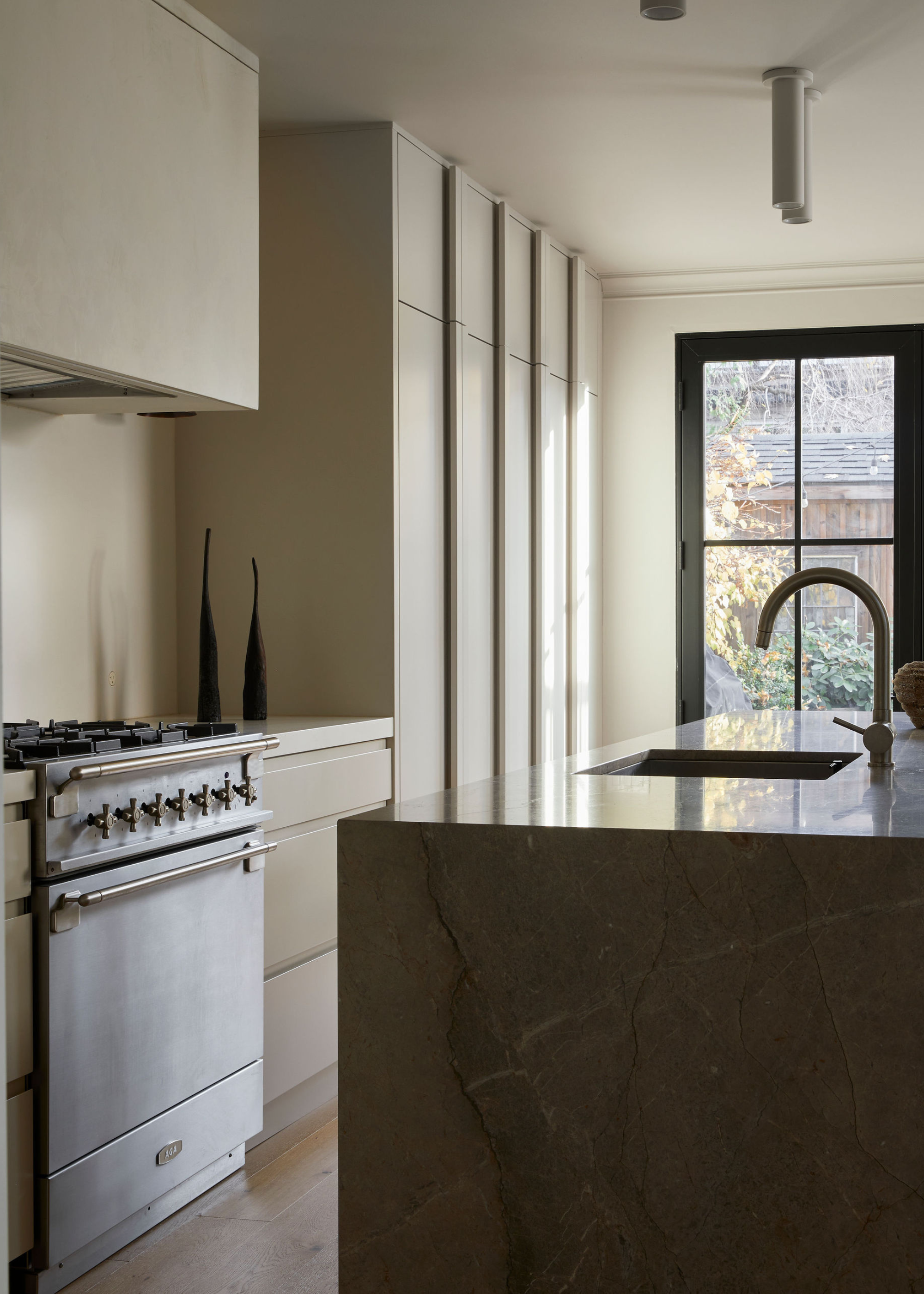 A minimalist kitchen with a marble island, off-white cabinets and stainless steel appliances