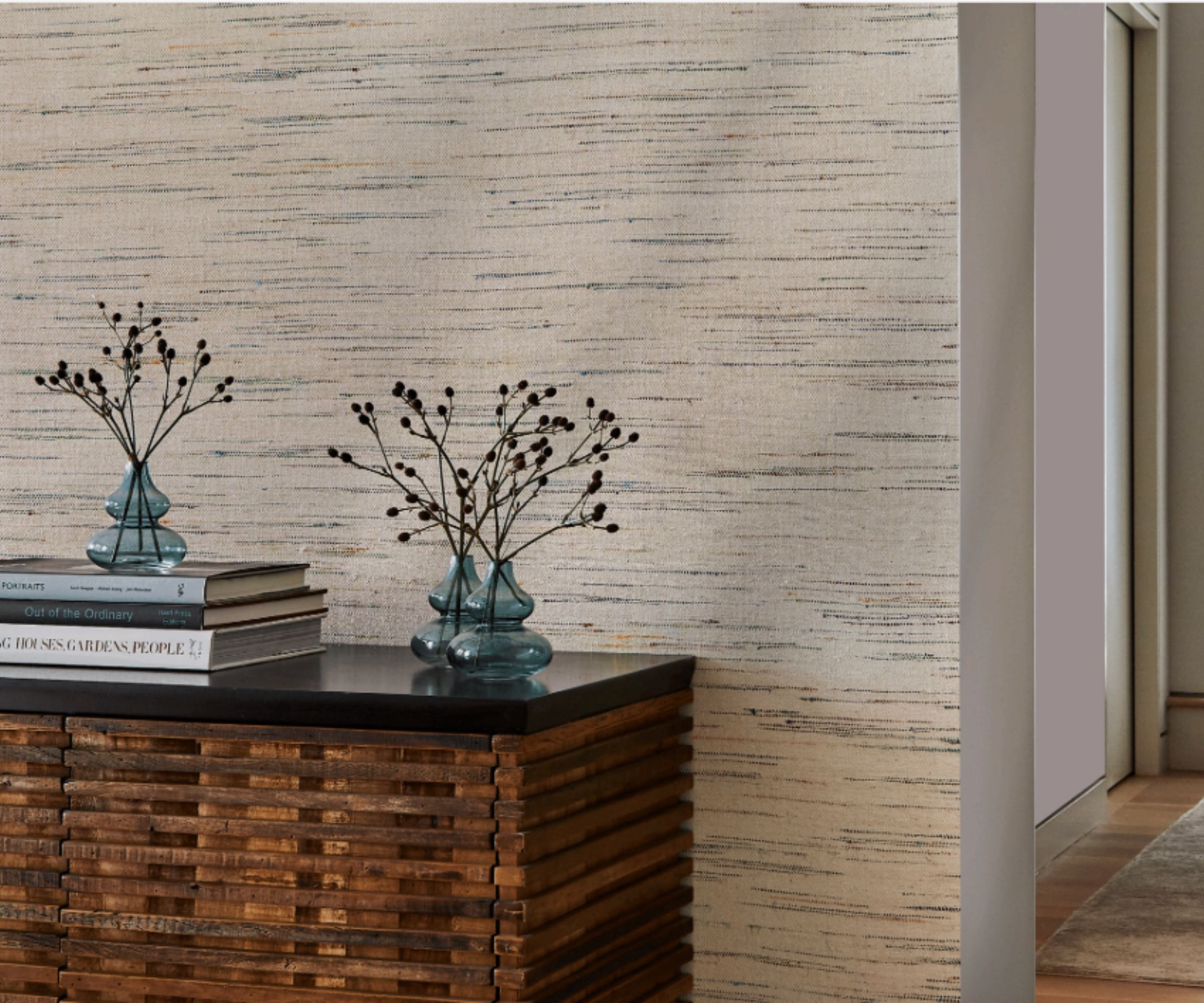 Close up of wooden console table decorated with vases and books, textured wallcovering behind, corridoor with wooden flooring to the right