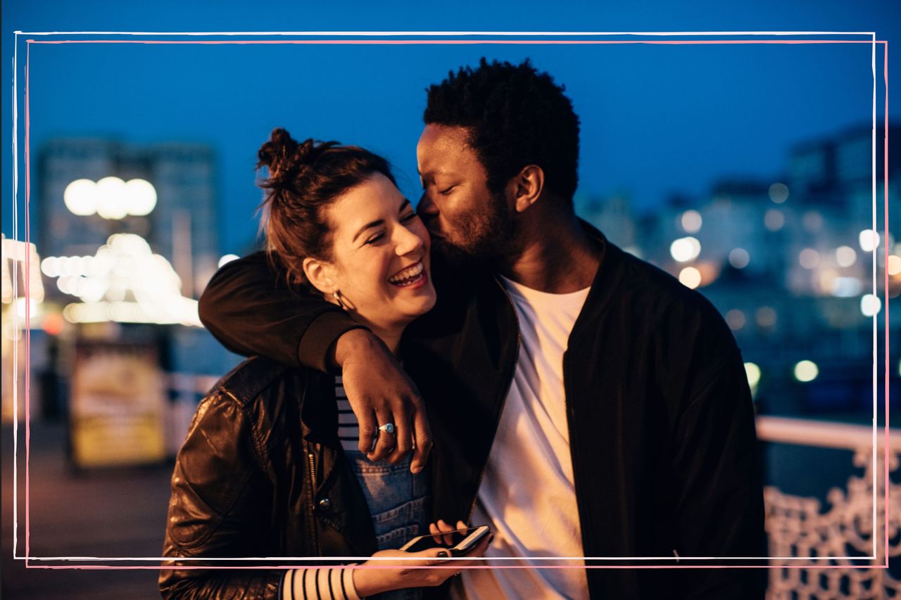 A happy couple with their arms round each other as the man kisses the woman on the cheek