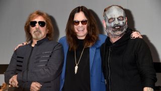 Corey Taylor standing on stage at a press event with Ozzy Osbourne and Geezer Butler
