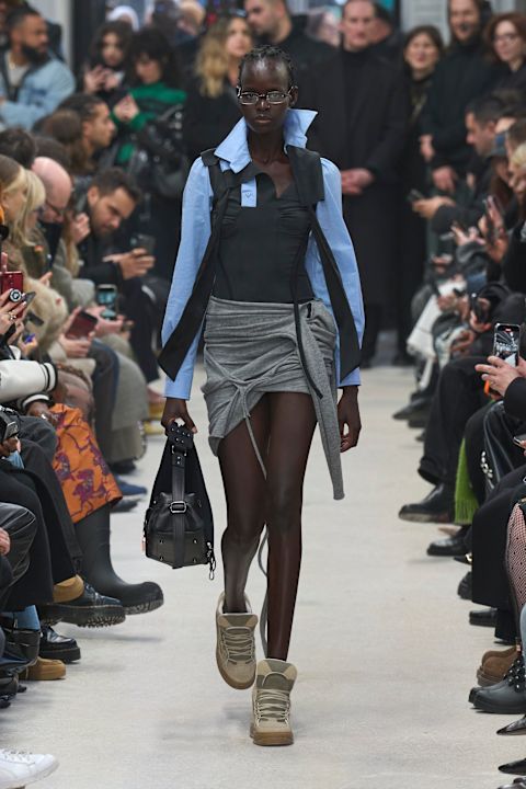An Ottolinger model wearig a blue longsleeve top, gray skirt, and tan wedge heel sneakers