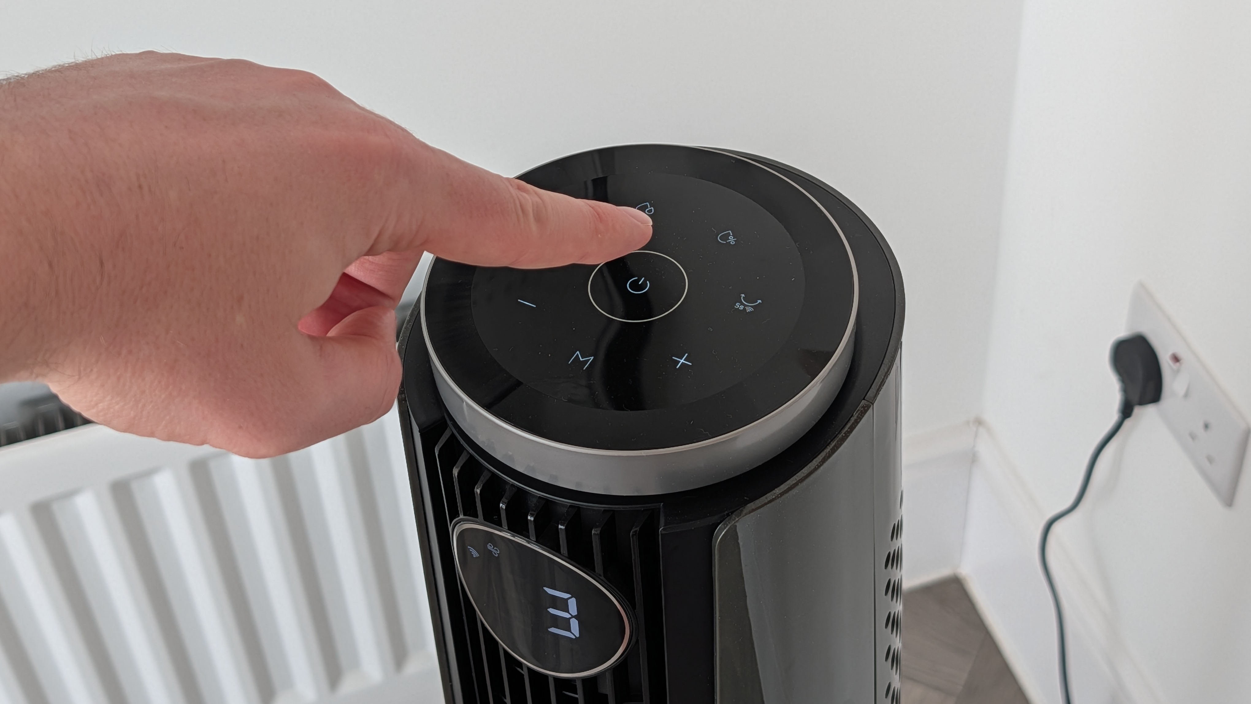 A man's hand reaching to press the off switch on the Dreo Smart Misting Fan 765S's controls.