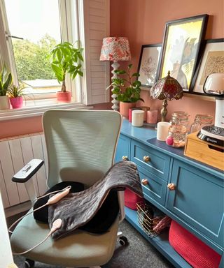 My gray heating pad on my pale green mesh office chair in a terracotta colored study with blue sideboard bobby lamp and white shutters in background