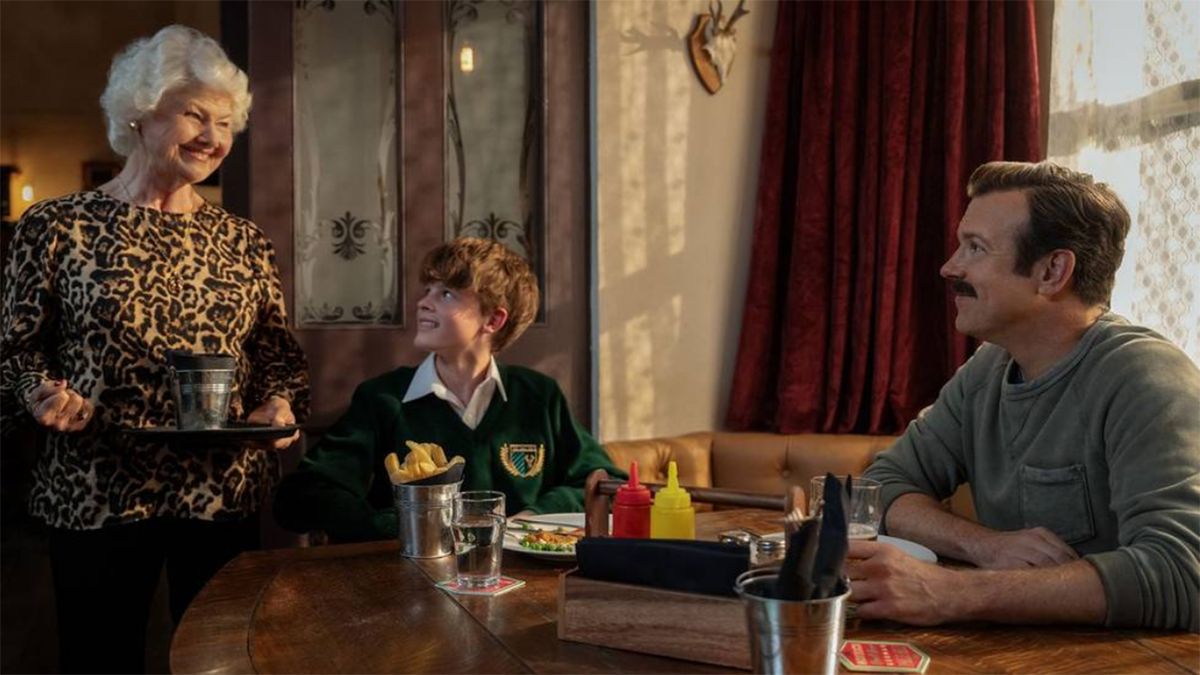 Mae smiling as she stands near a seated Henry and Ted in Ted Lasso season 4
