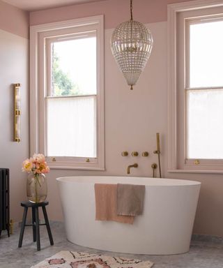 glass chandelier hanging over modern freestanding bath in bathroom painted pink