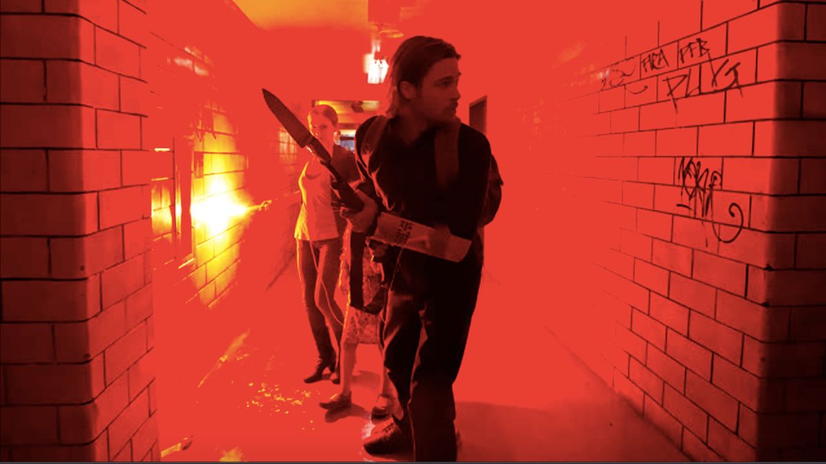 Mireille Enos and Brad Pitt walking down a hallway with a flare in World War Z.