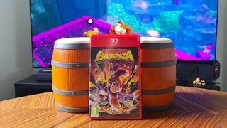 Donkey Kong Bananza game box leaning against Donkey Konga Bongos controller for GameCube with TV in backdrop featuring gameplay.