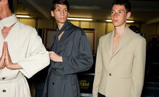 Three guys wearing the JW Anderson S/S 2015 collection. On the left the guy is wearing a beige overcoat with a matching scarf. Next to him, the guy is wearing a gray overcoat with matching scarf. On the right, the guy is wearing a beige jacket with one button.