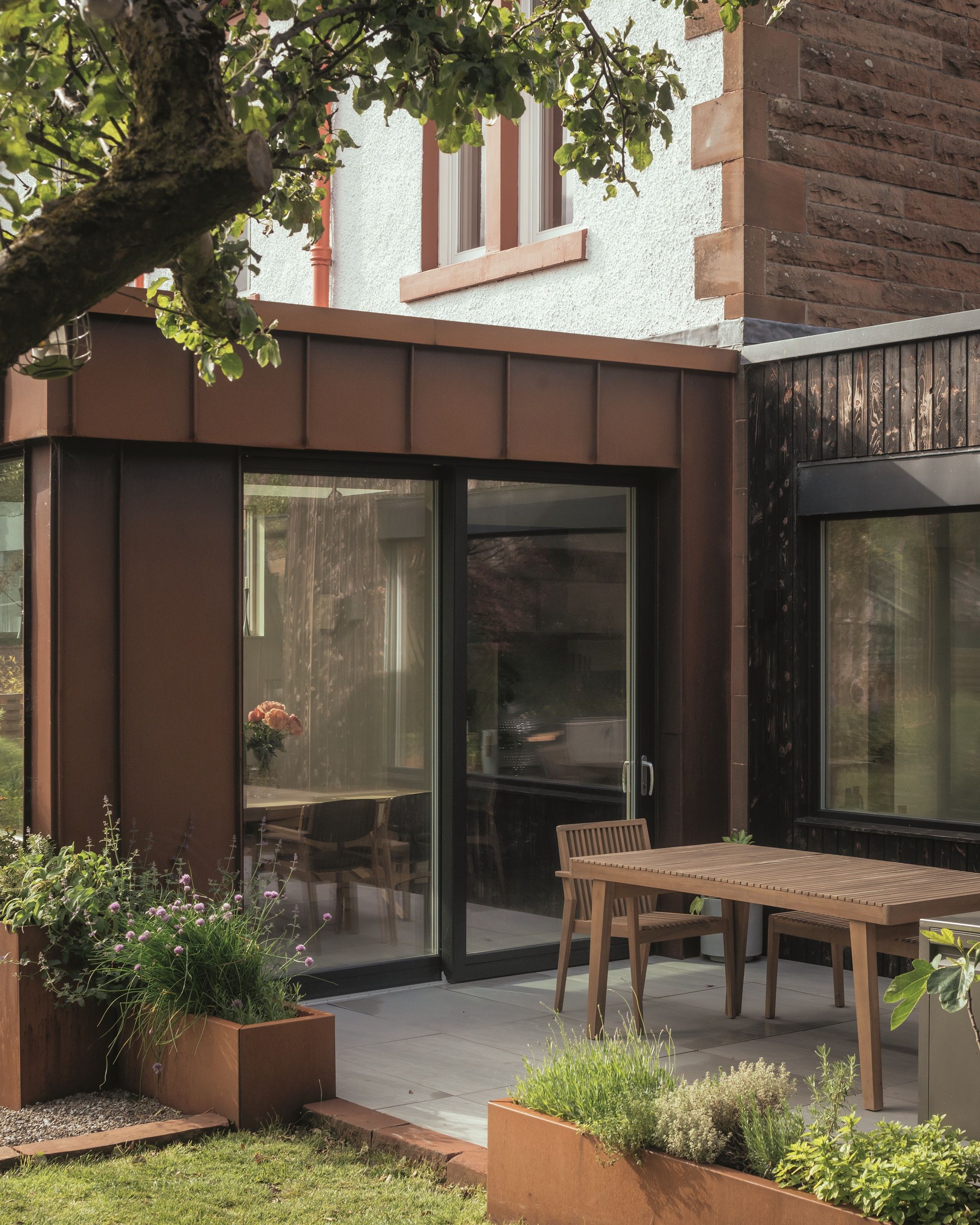 red brick extension with built-in planters, outdoor dining area, and large sliding doors