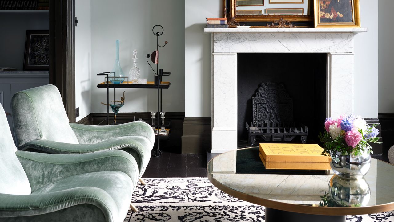 A living room with a marble fireplace, sage green velvet chairs and a patterned rug