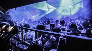 The view from the DJ booth at Fabric London, showing the crowd on the dance floor bathed in blue light.