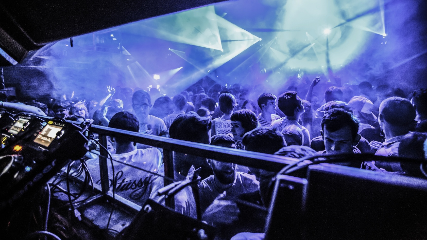The view from the DJ booth at Fabric London, showing the crowd on the dance floor bathed in blue light.