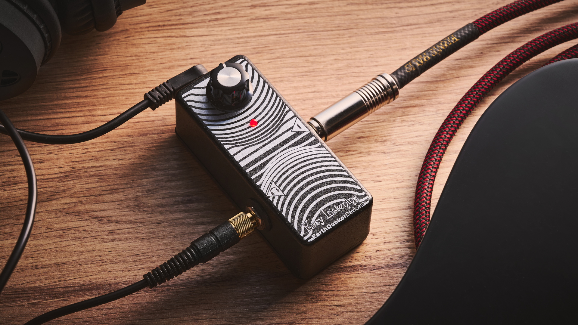 An Earthquaker Devices Easy Listening headphone amp for guitar on a wooden floor with a guitar cable and headphones plugged in