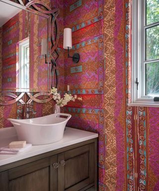 An example of powder room wall decor showing a bright pink powder room with a wooden sink stand and a white sink