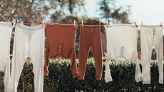 A clothes line hung outside in front of a green hedge with orange and white cotton pyjamas hanging from it