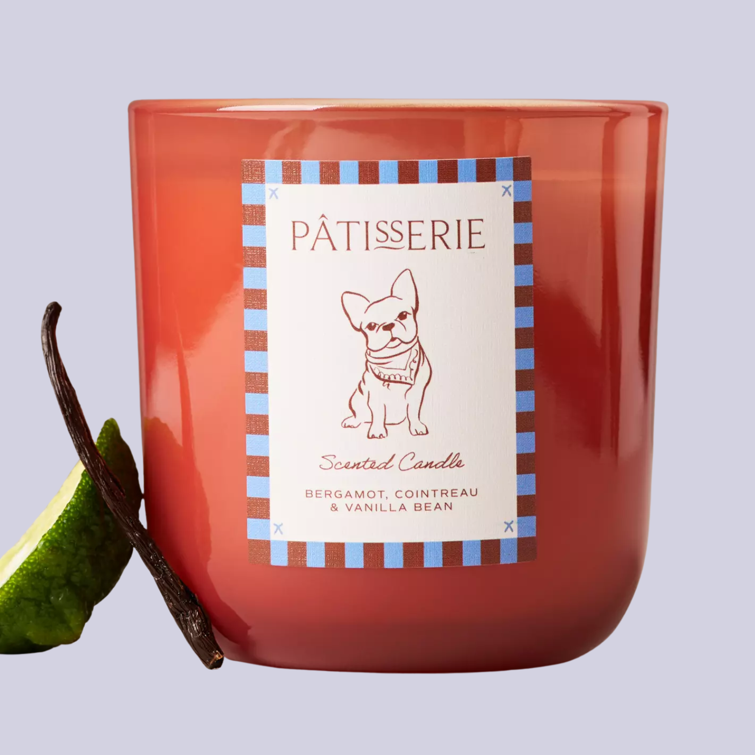 A pink glass candle with a vanilla bean and a bergamot slice