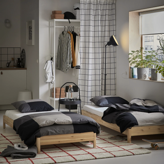 two Scandi-style stackable bed and sofas with dark black and gray bedding on top, a black and white square curtain, a window, and a red and white square rug on the floor