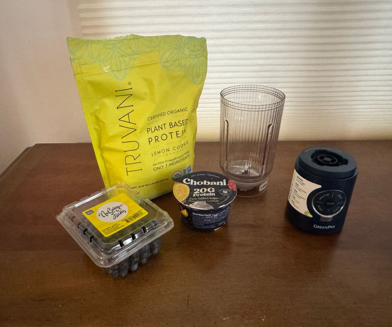 A bag of protein powder, a yogurt, and some blueberries beside a small portable blender.