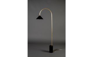 Floor lamp with black head and base connected by gold metal stand, photographed against a grey background