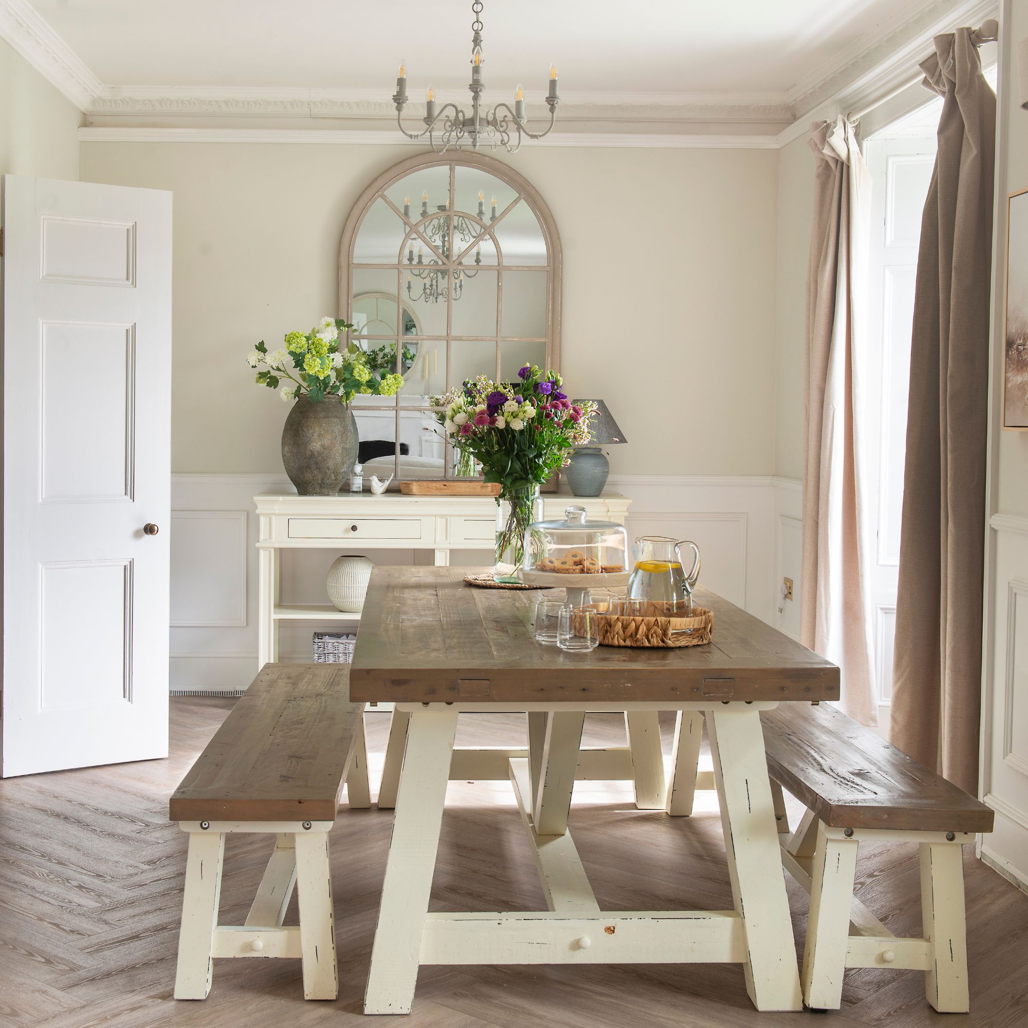 Dining room in cottage with wooden table and benches, wooden floor and window mirror