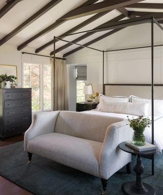 bedroom with beamed vaulted ceiling, four poster and white end of bed sofa