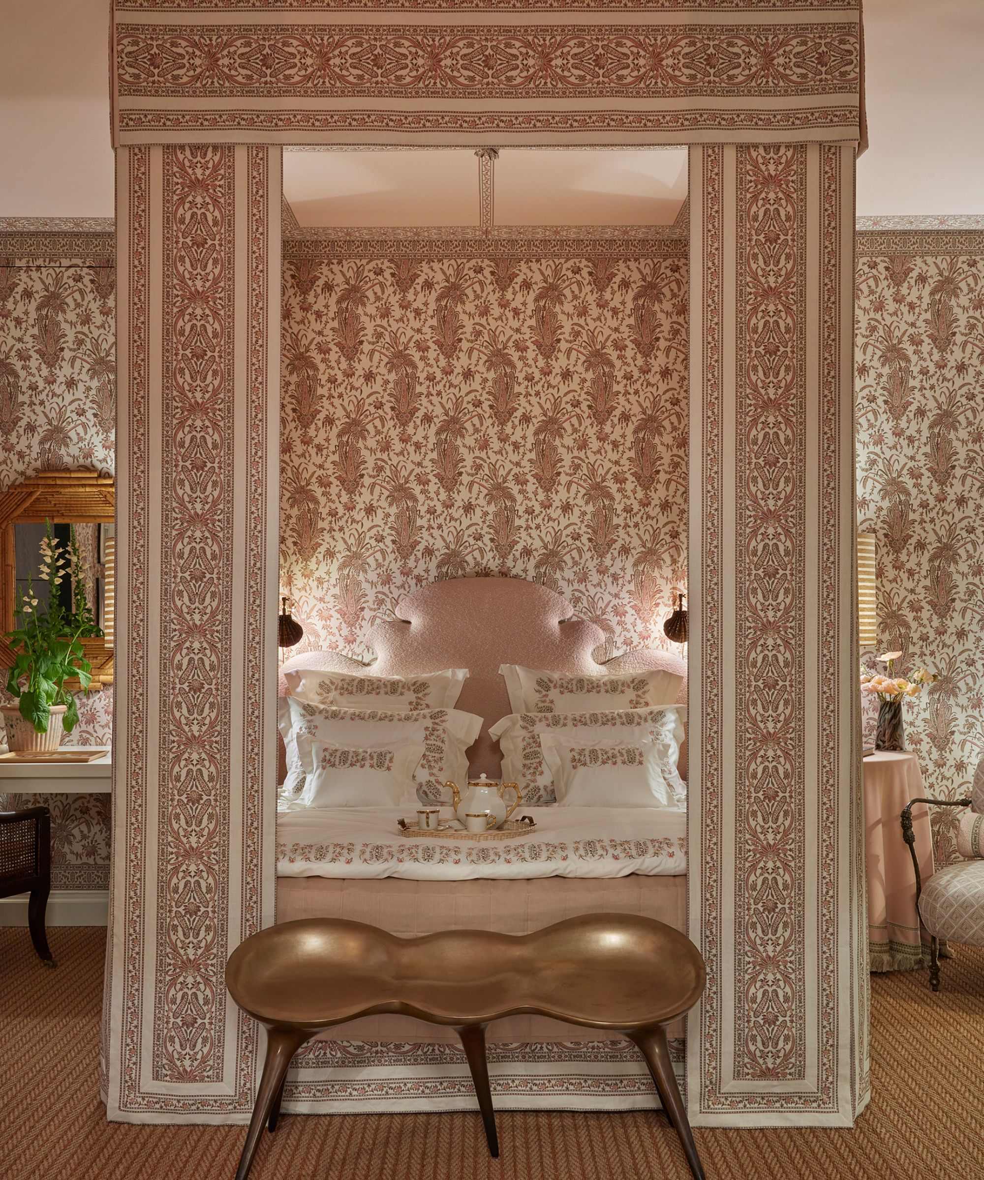 A bedroom with pink floral wallpaper, sisal carpet and a four poster pink bed with a pink headboard
