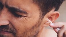 Man trying to clean his ears with a cotton bud